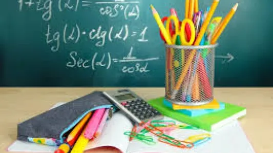 Fournitures scolaires posées sur un bureau devant un tableau